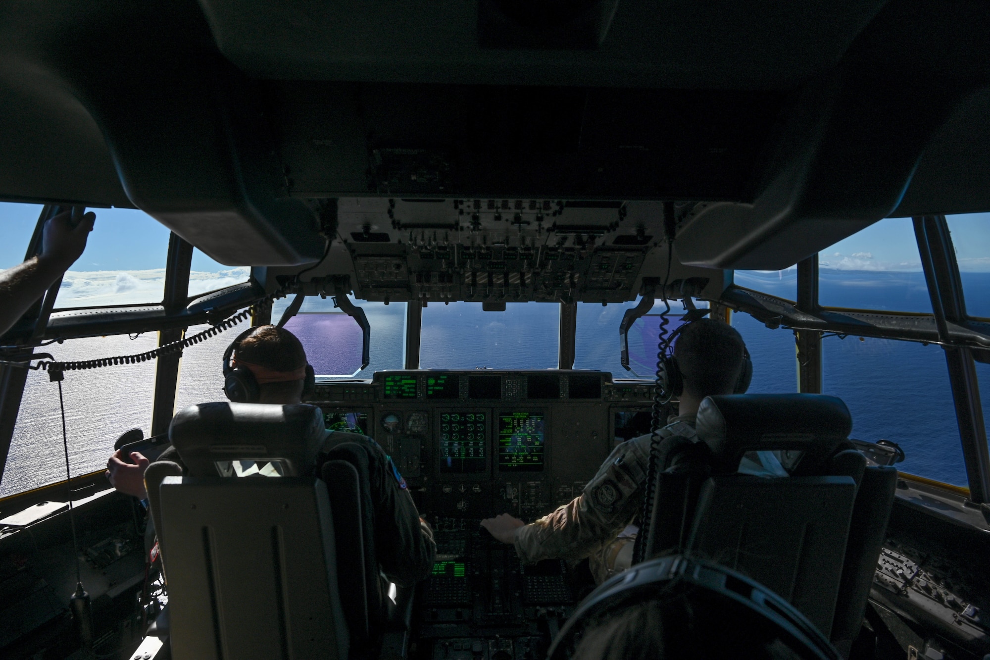 Two U.S. Air Force pilots sit in the cockpit and pilot a C-130J aircraft over open water.