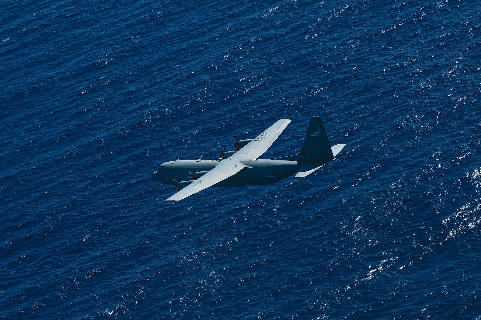 A C-130J aircraft soars over open waters.