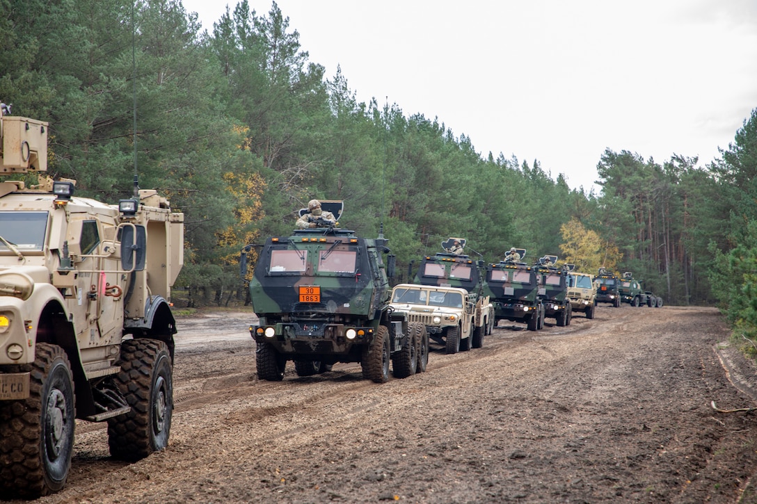 Military vehicles drive down a dirt road.