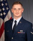 Airman 1st Class poses in uniform for an official photo in front of the American flag.