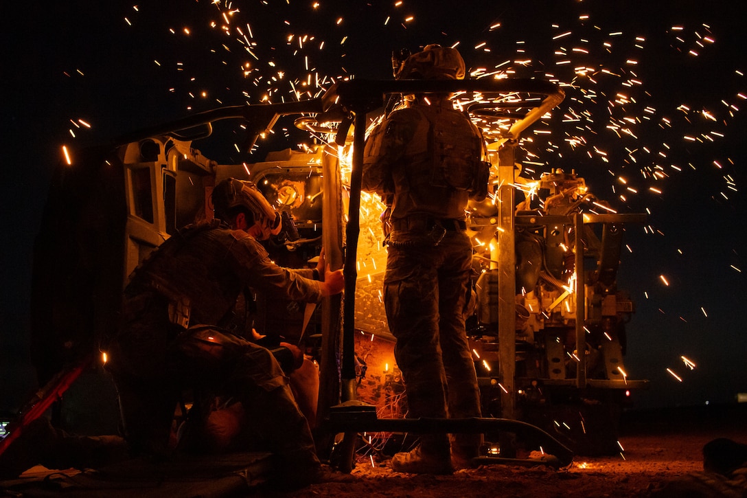 Airmen cut into a military vehicle during night training. Yellow sparks can be seen flying from the vehicle.