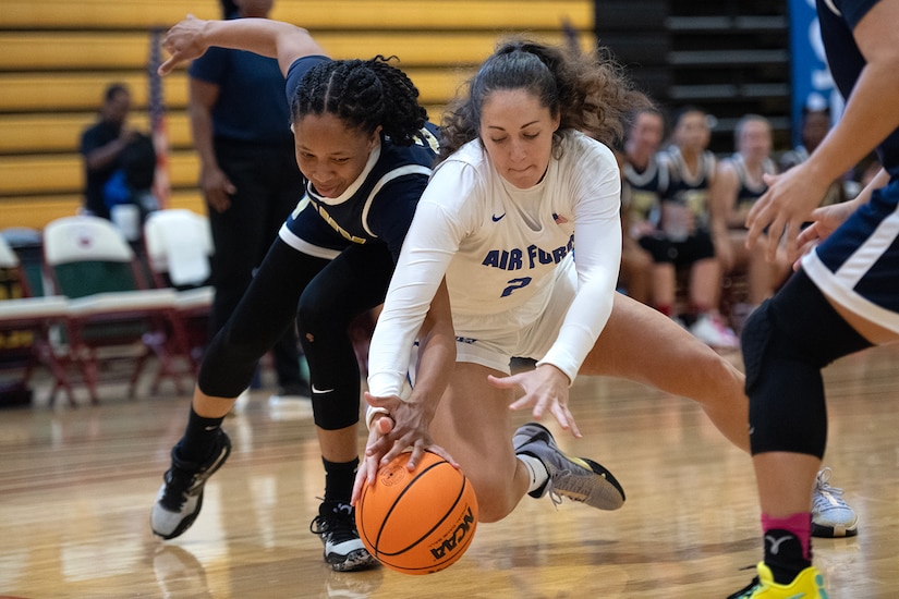 An airman and a sailor battle for a loose basketball.