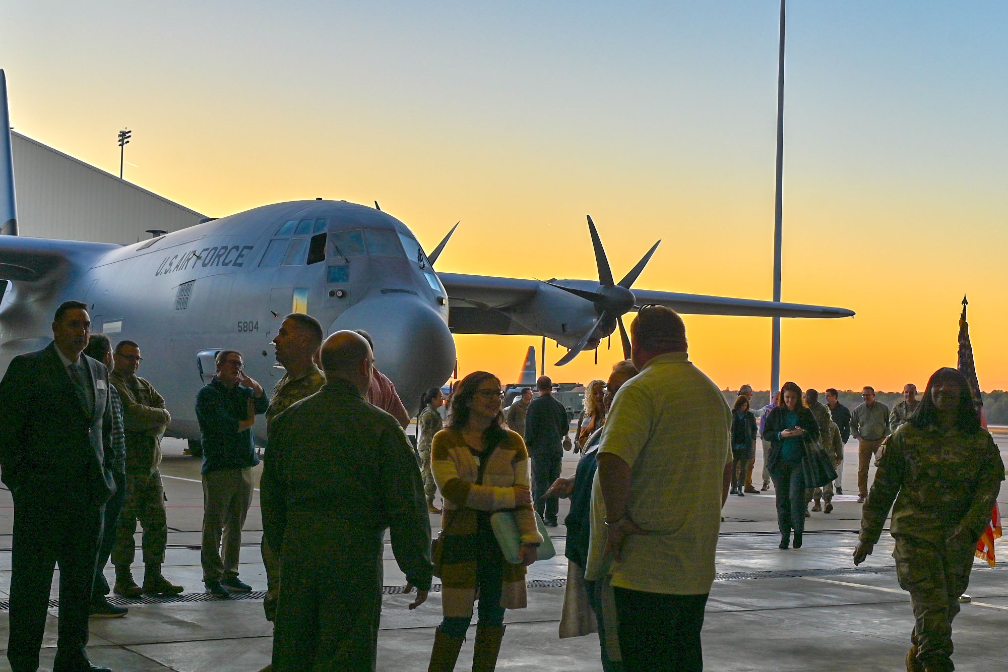 U.S. Airmen and civilians stand in front of a C-130J aircraft.