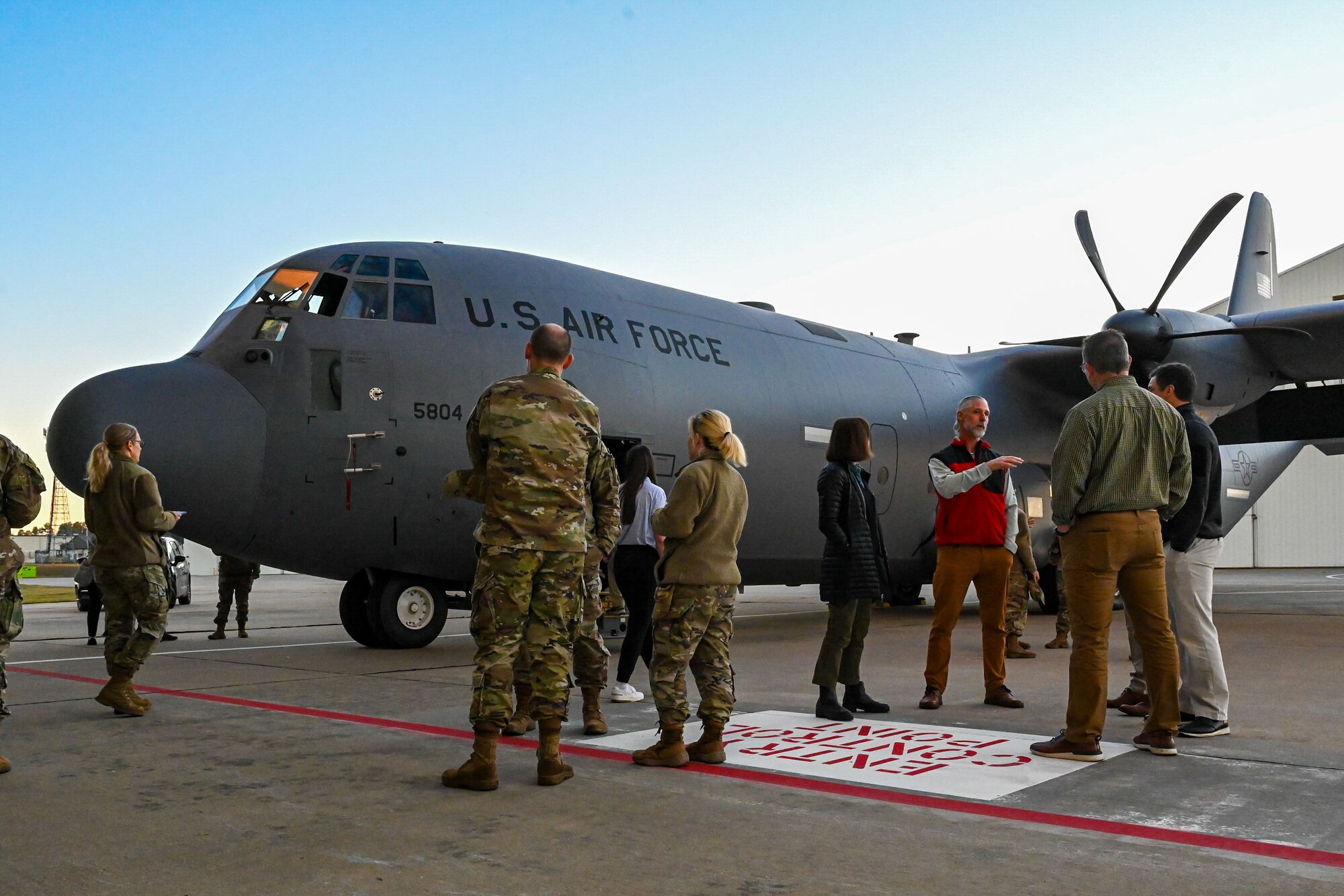 U.S. Airmen and civilians stand in front of a C-130J aircraft.