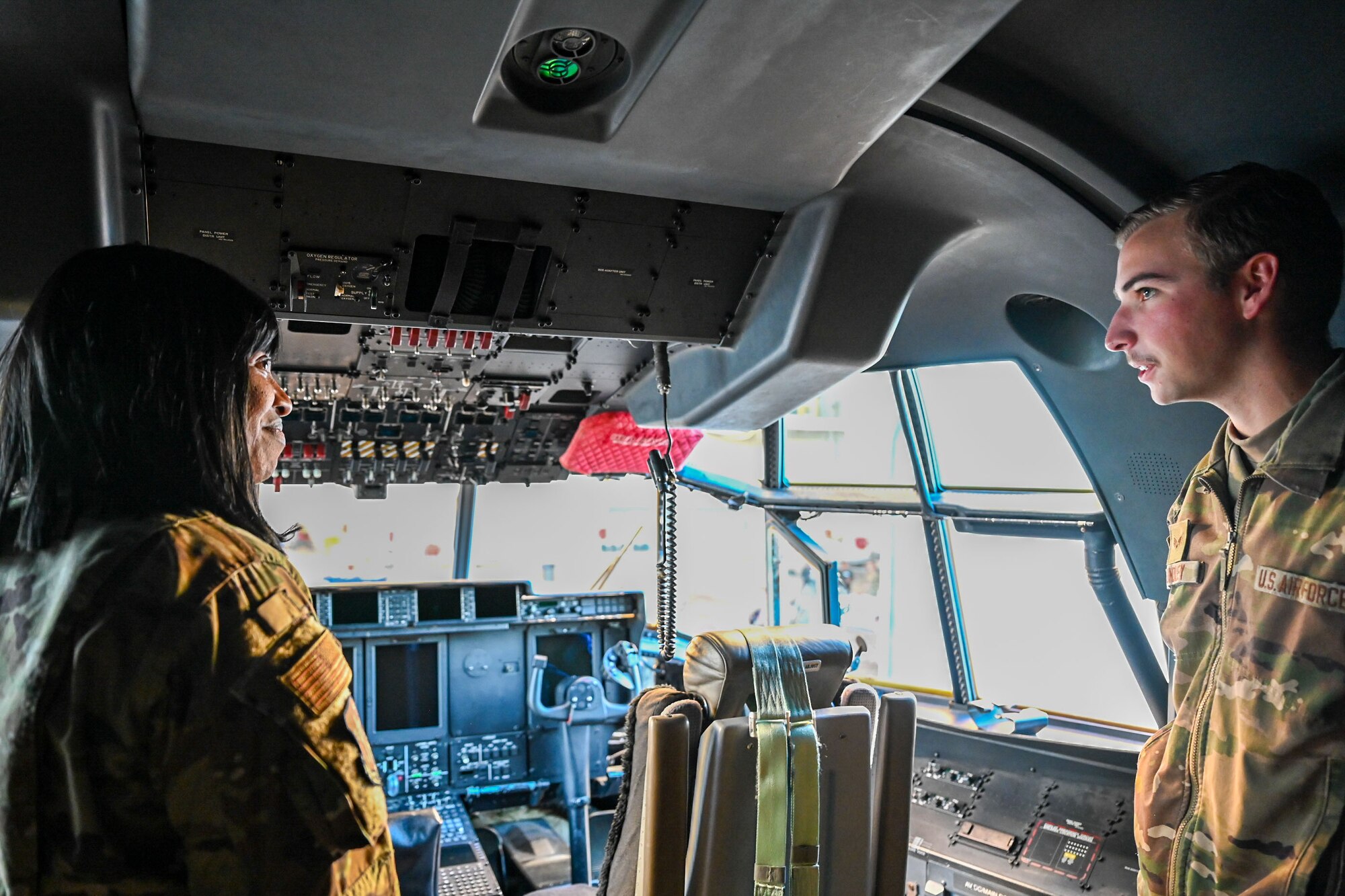 Two U.S. Airmen stand in the cockpit of a C-130J aircraft.