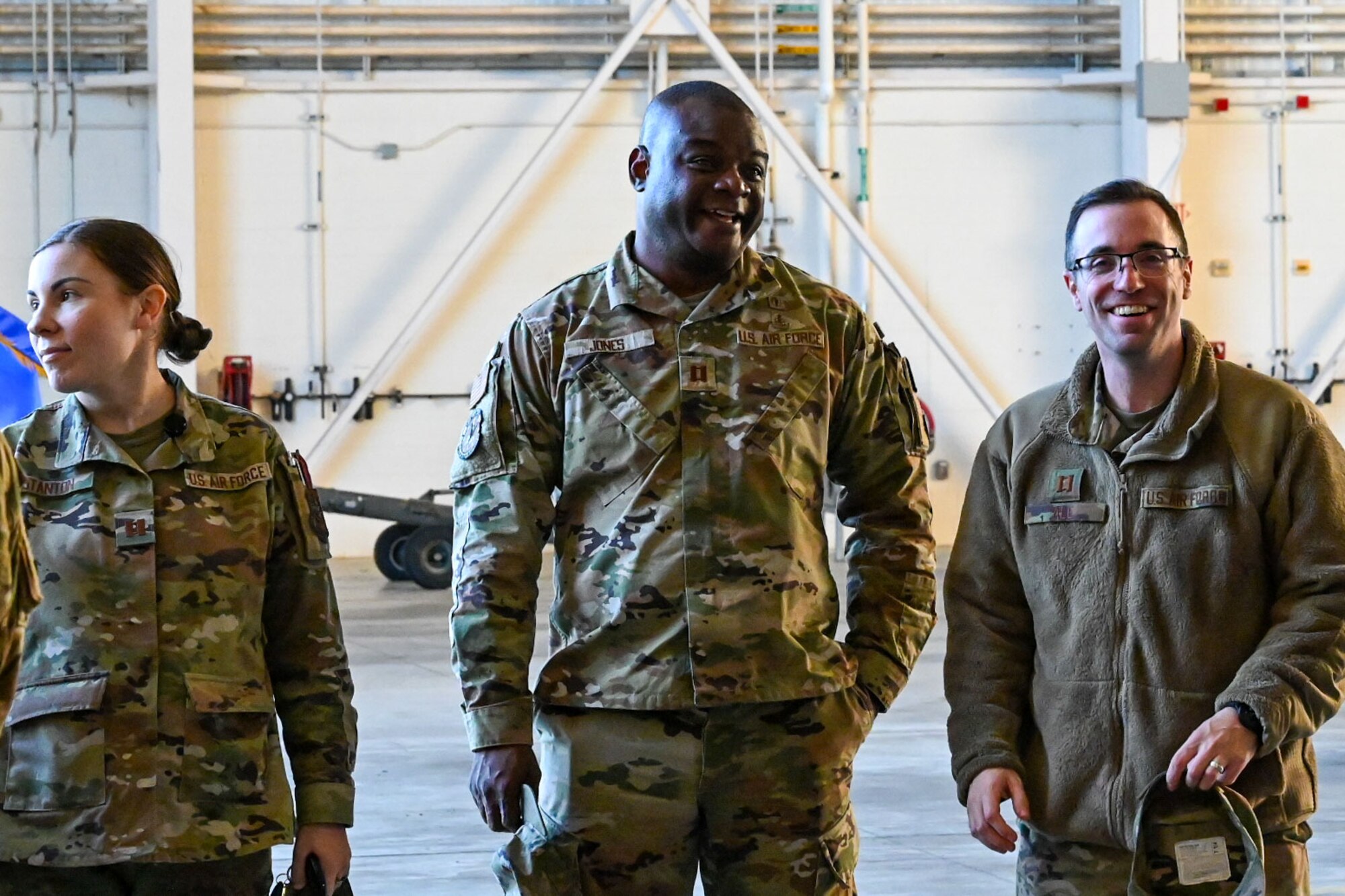 Three U.S. Airmen stand inside a hangar.
