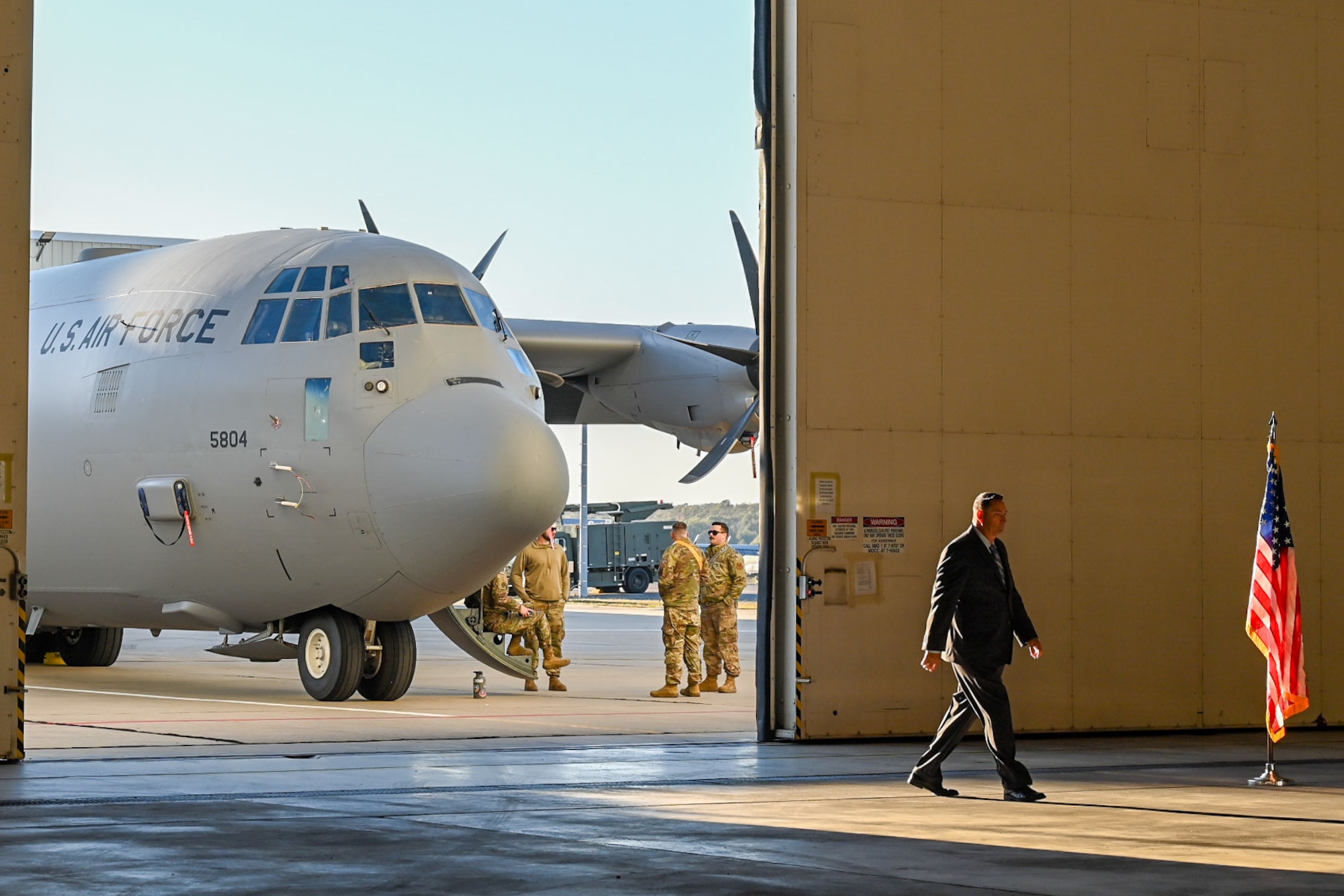 A man walks into a hangar with a C-130J aircraft in the background.