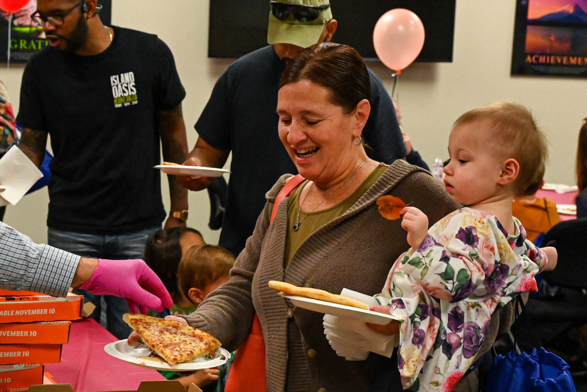 A woman holds a baby as she is served pizza.