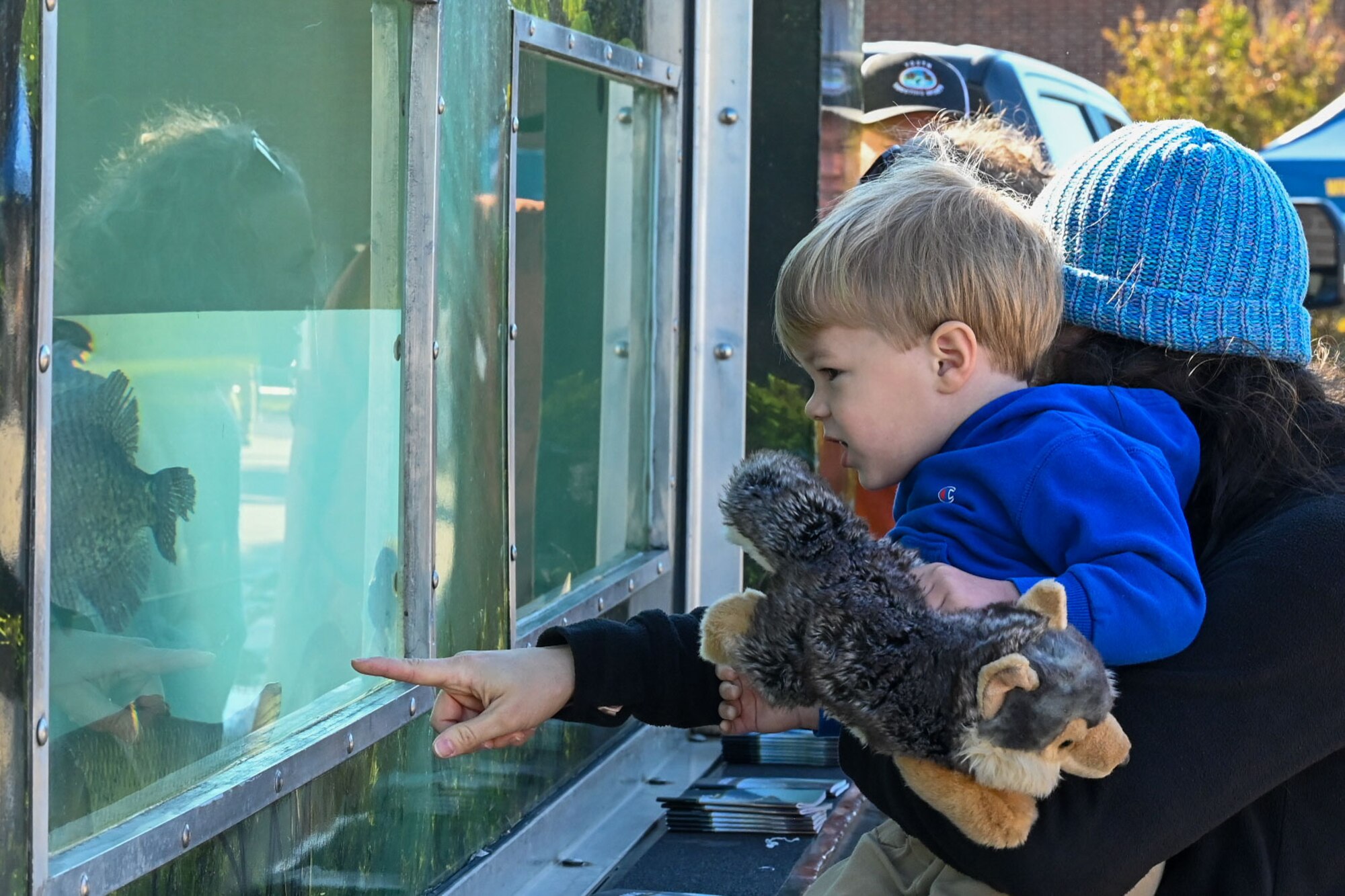 A woman holds a child in her arms as they look into a fish tank.