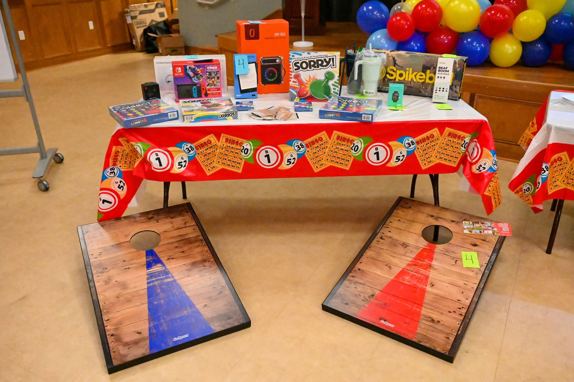 Two cornhole boards sit in front of a table with prizes on it.