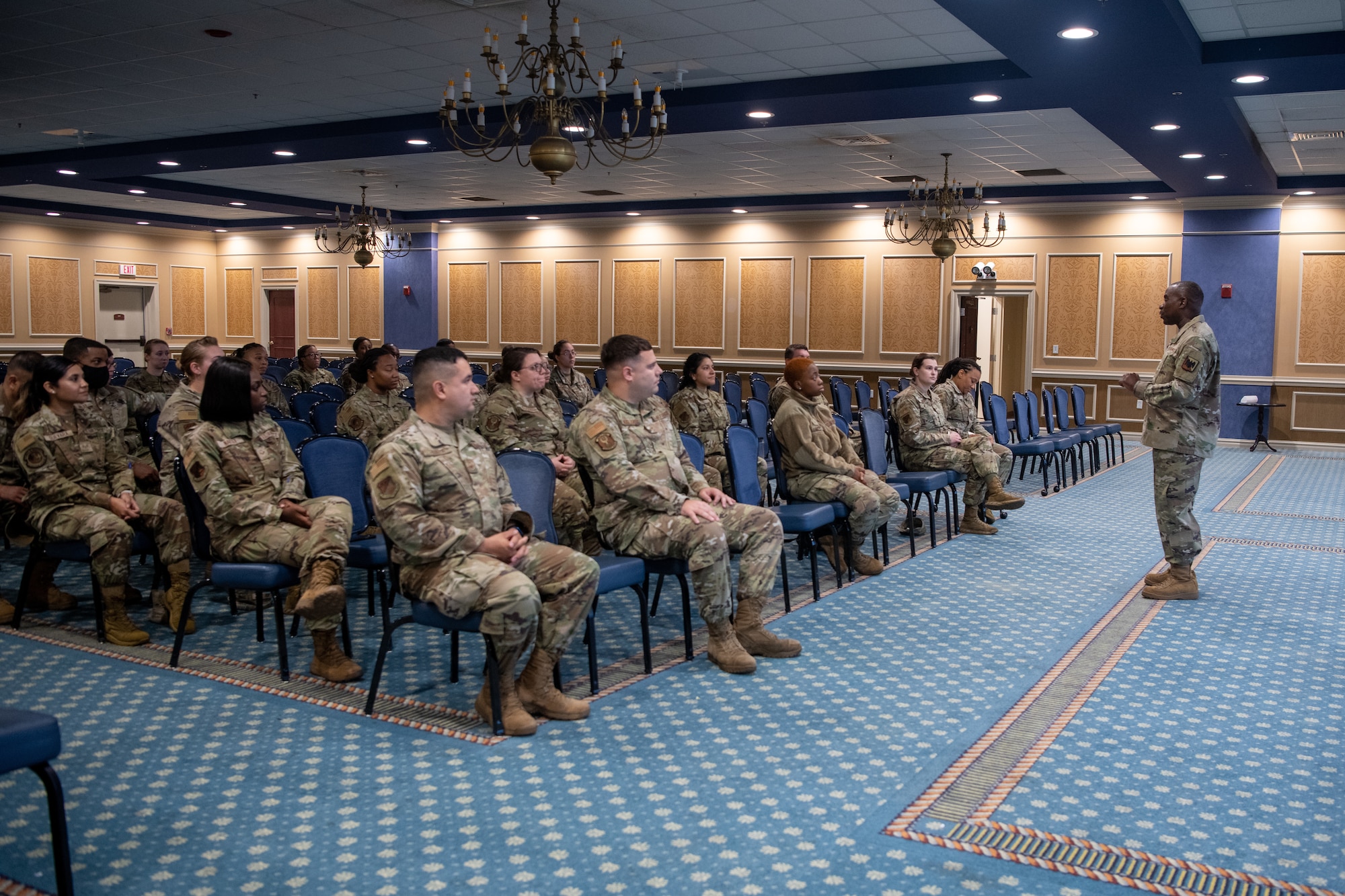 Group of Airmen sitting in chairs on left, Chief Williams standing on right.