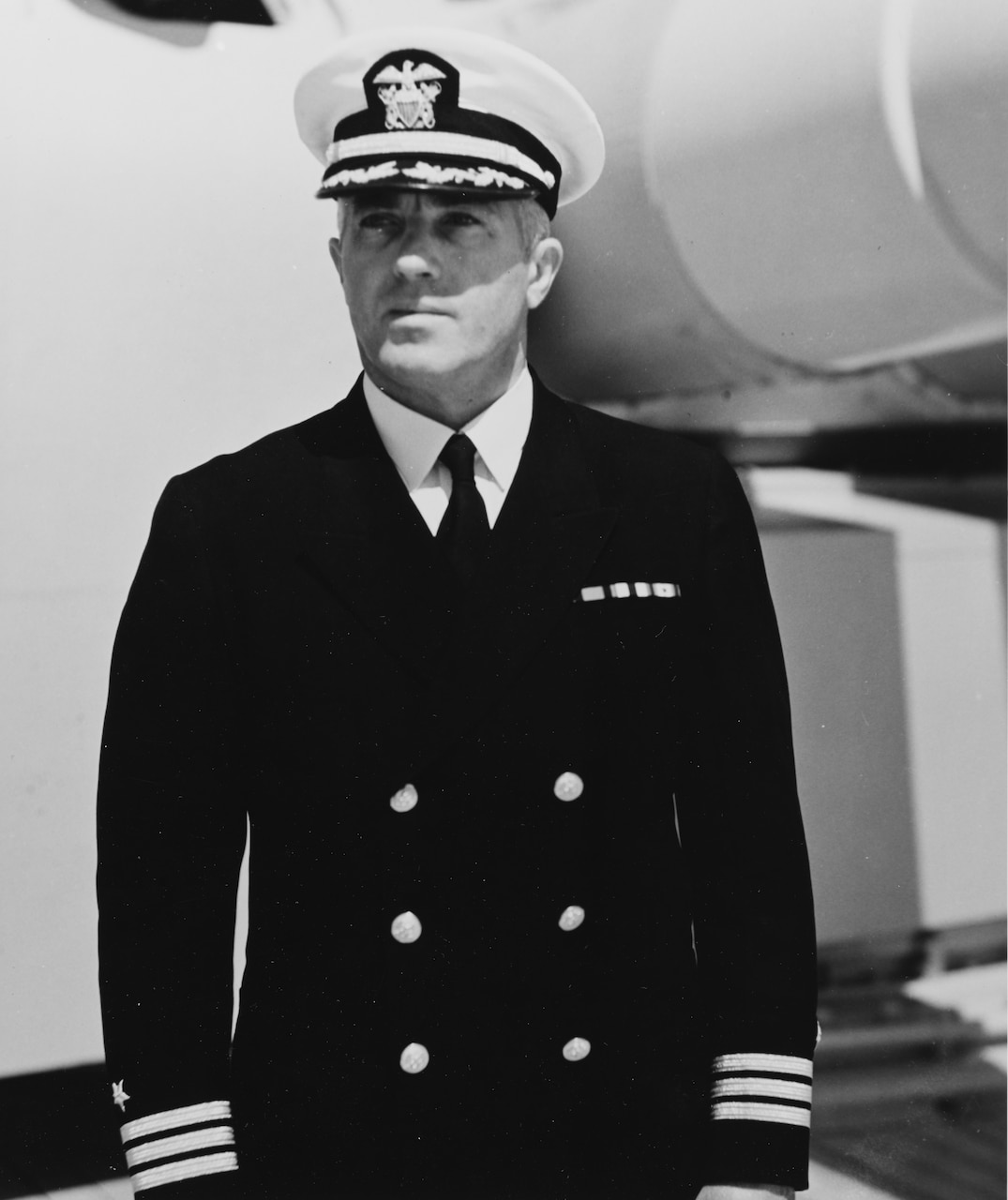 A man in dress uniform and cap looks into the distance.