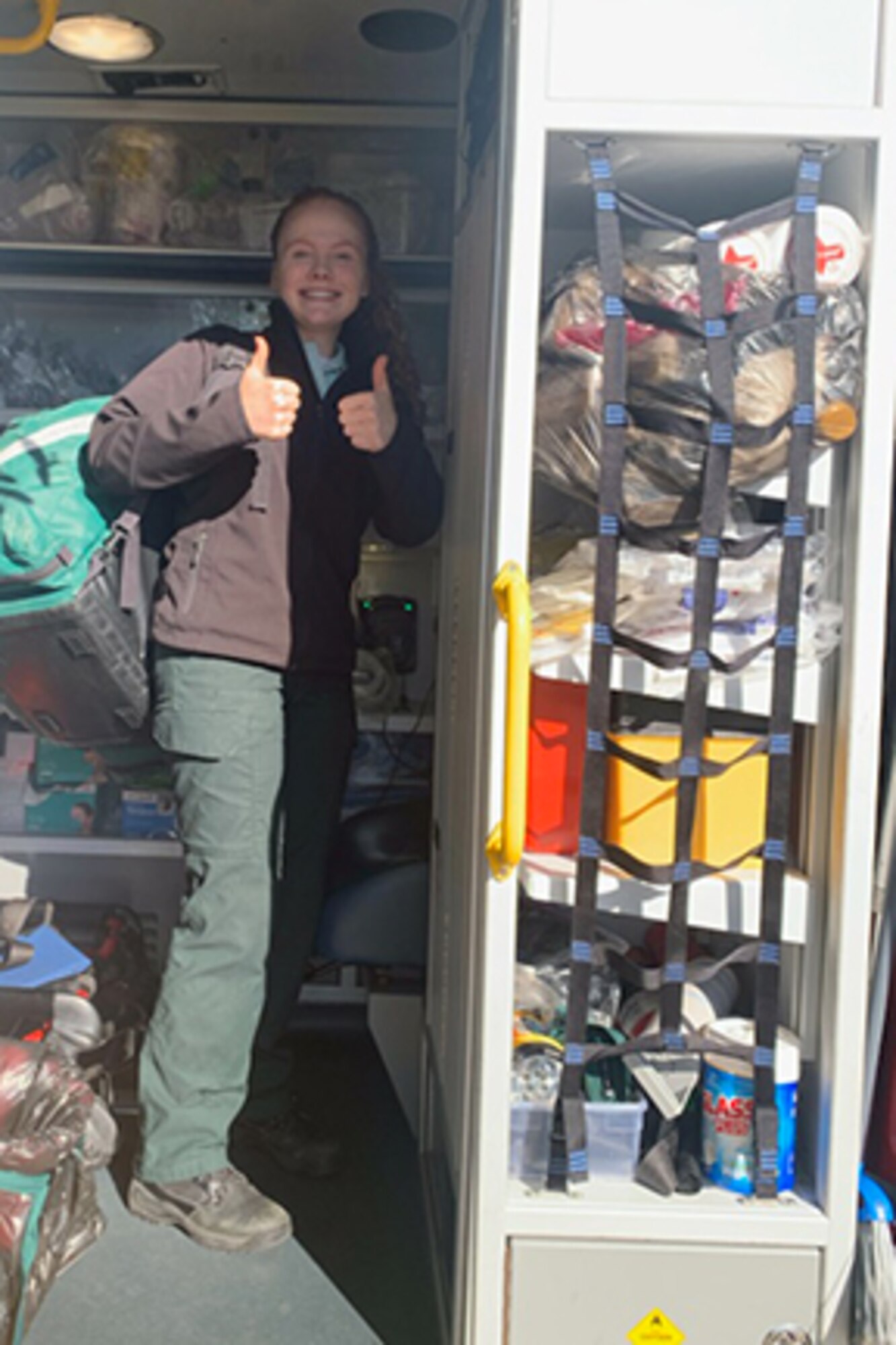 Capdepon stands inside of an emergency response vehicle, with two thumbs up and a smile on her face while surrounded by EMT equipment and gear.