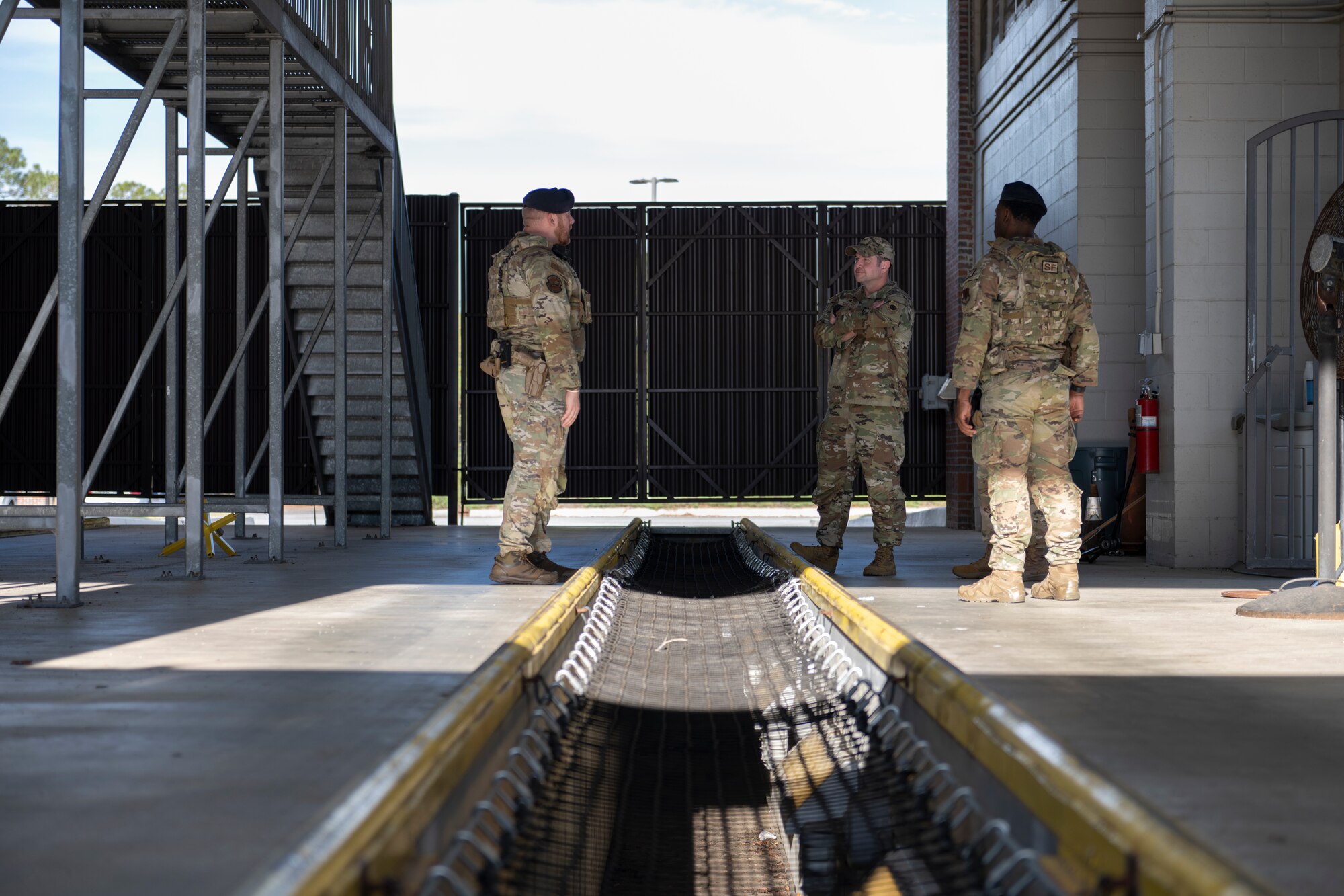A photo of three people standing in a big warehouse with ladders and a placed to crawl under vehicles.