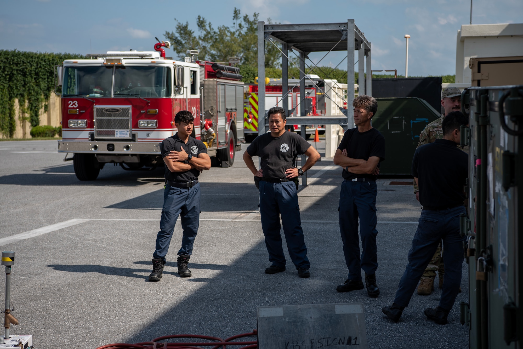 Fire fighters observe demonstration in front of firetrucks.
