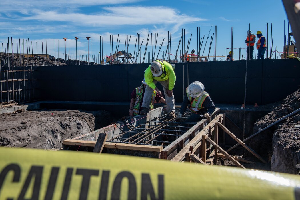 Two men stand over a rebar frame on a construction site.