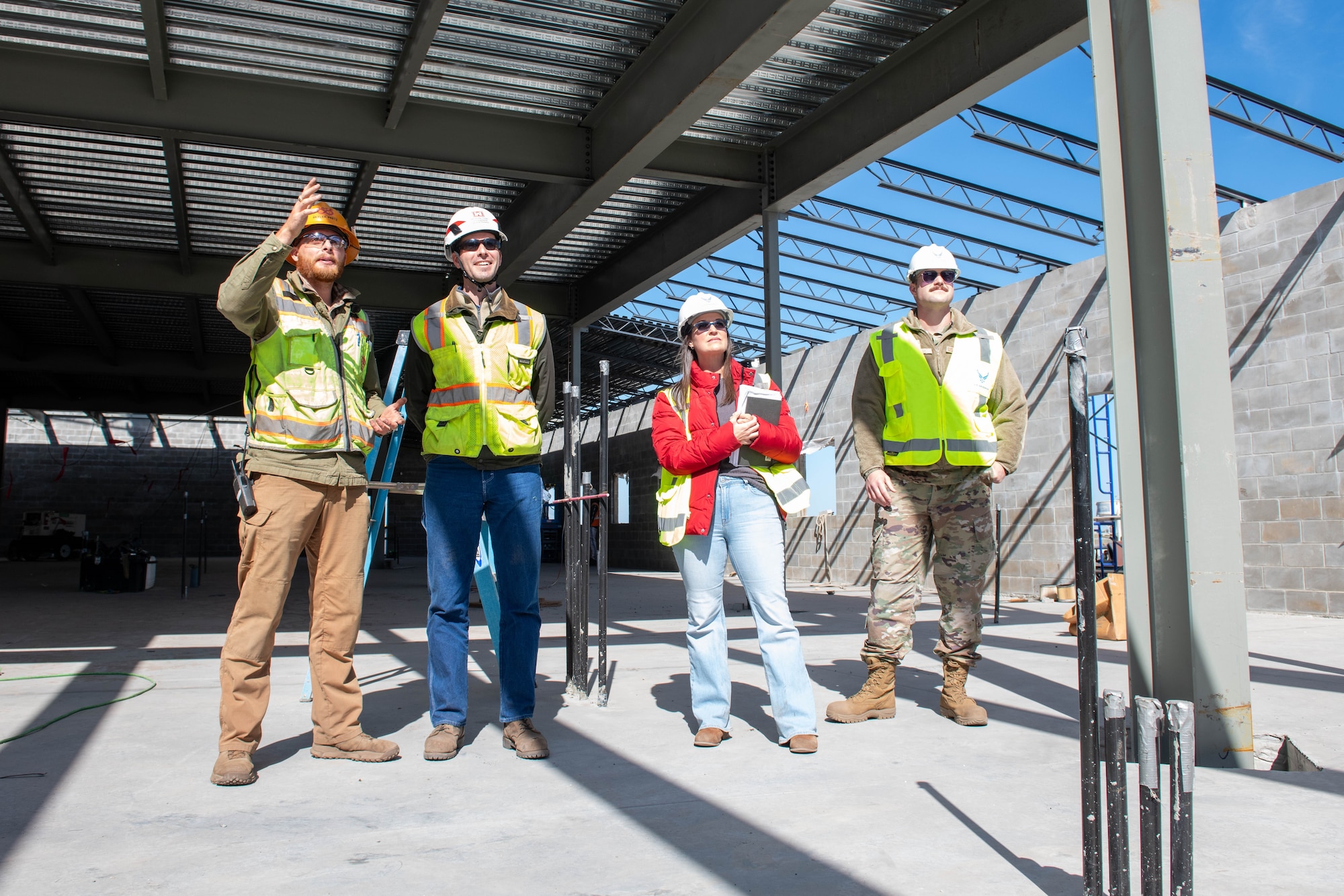 Four engineers stand in a facility that is being constructed to observe the progress that has been made.