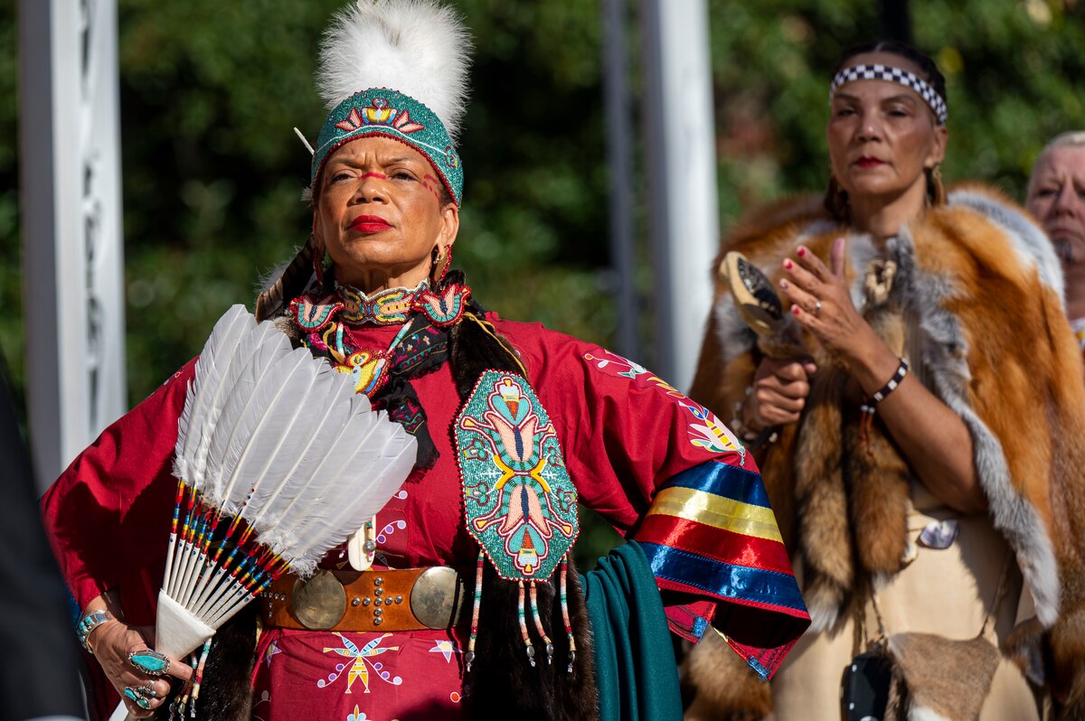 Two dancers in traditional native clothing stand outdoors.