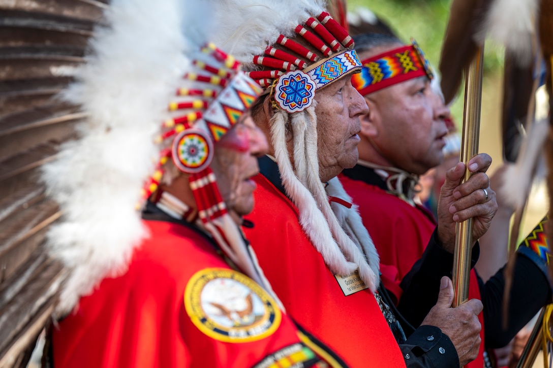 Native Americans stand next to each at attention during a ceremony.