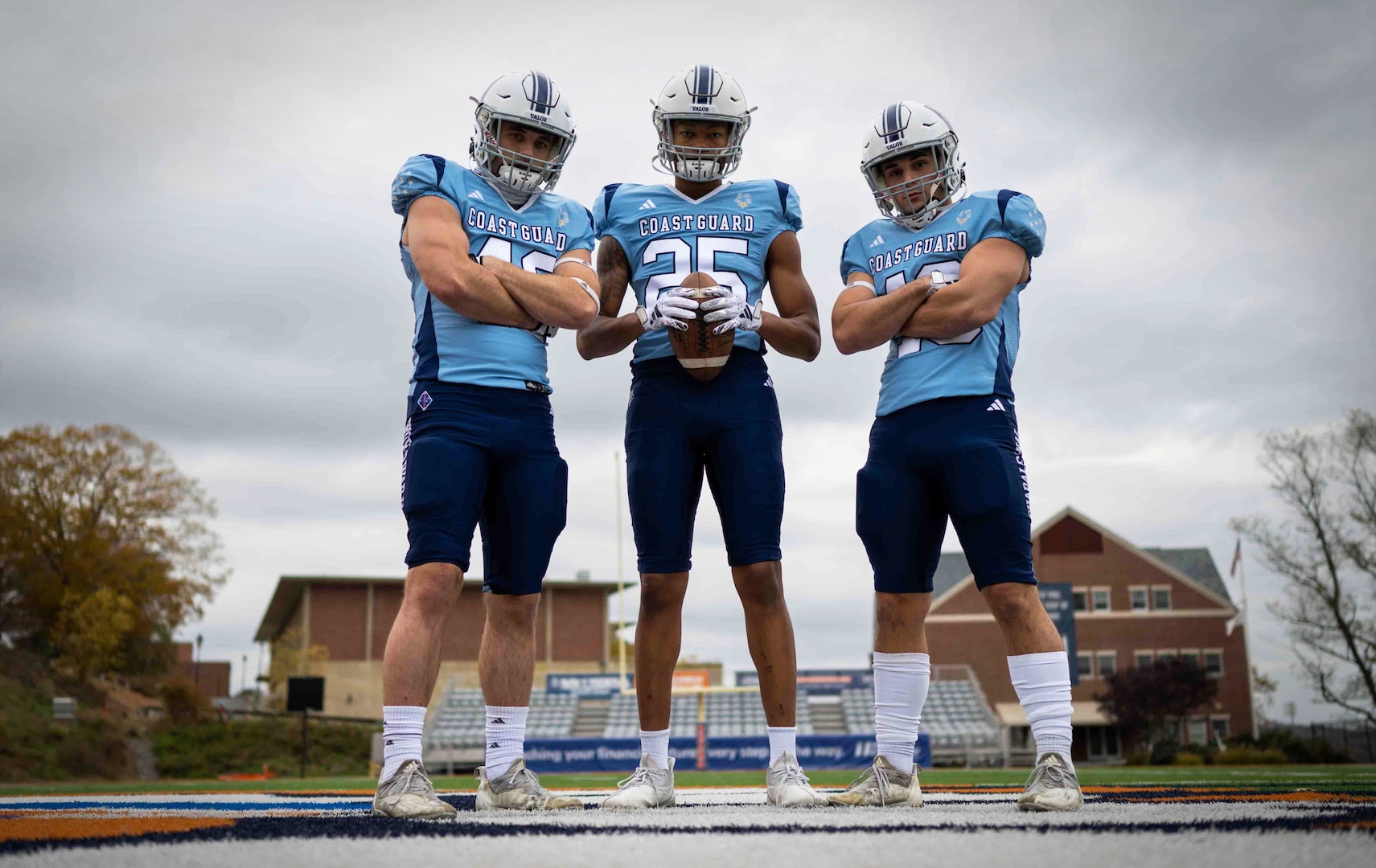 3 Cost Guard Academy cadets in their football uniforms posing in front of the camera showing off their new uniforms.