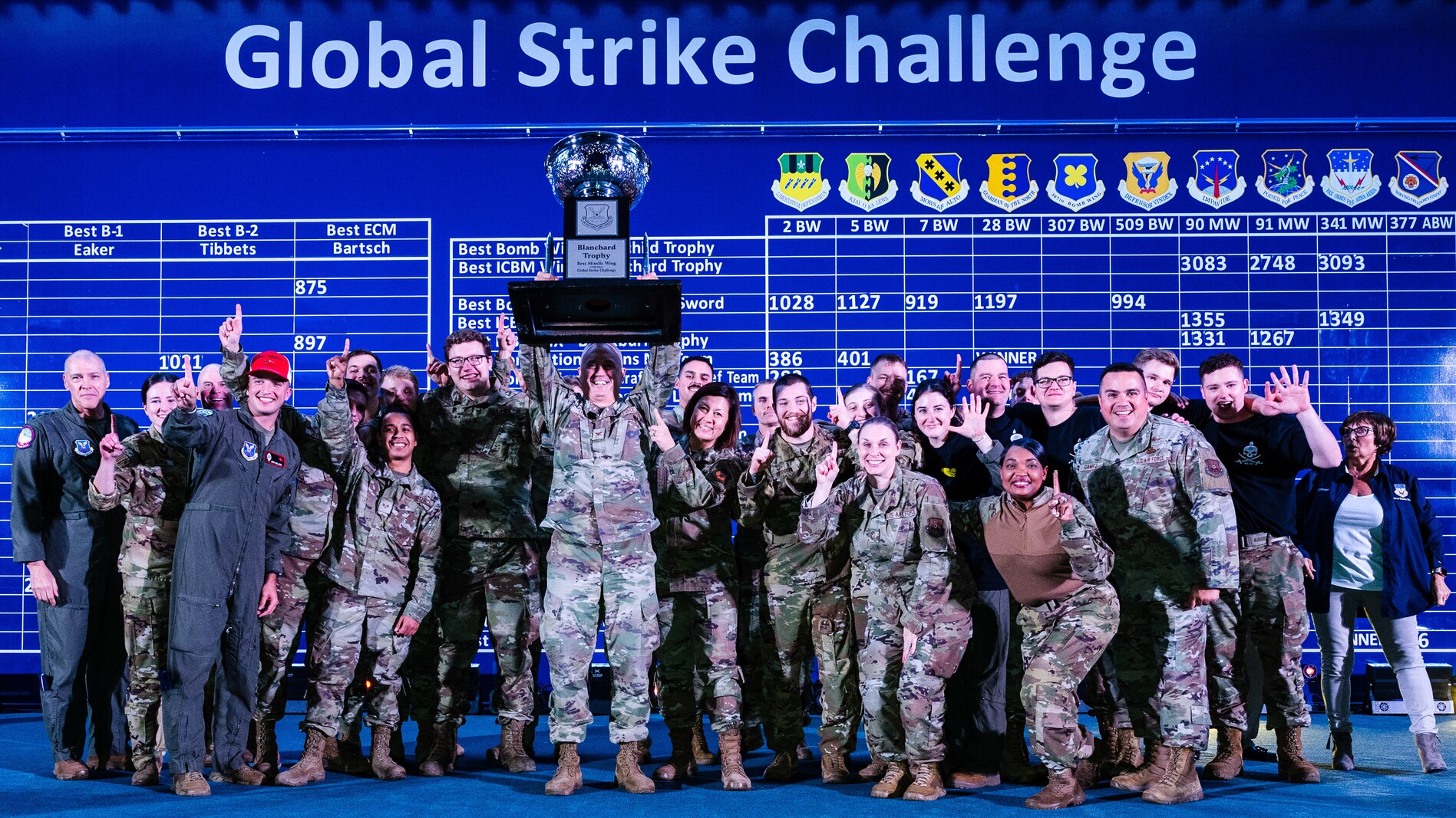 A large group photo of uniformed Air Force personnel who are celebrating by holding a large trophy up.