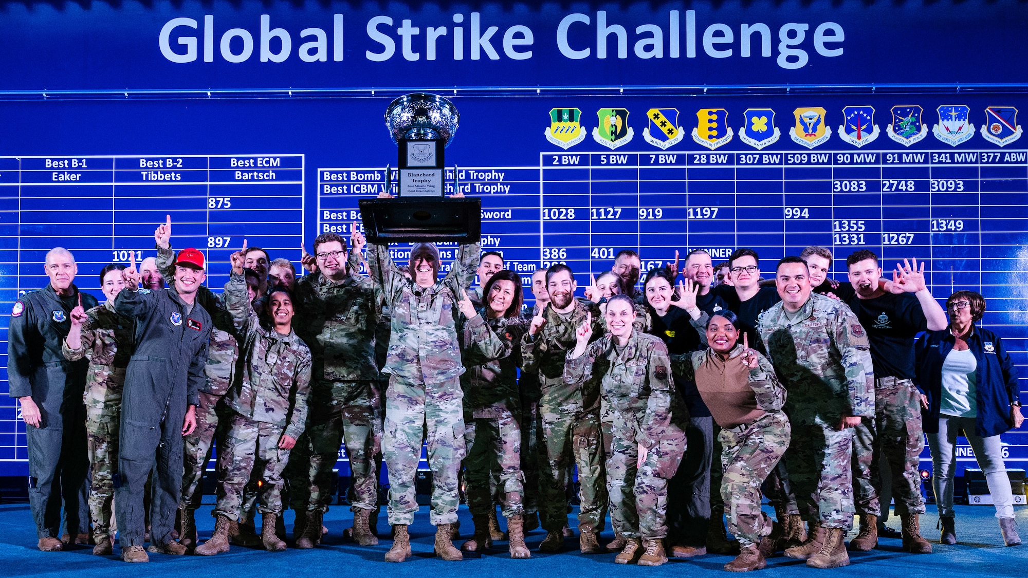 A large group photo of uniformed Air Force personnel who are celebrating by holding a large trophy up.