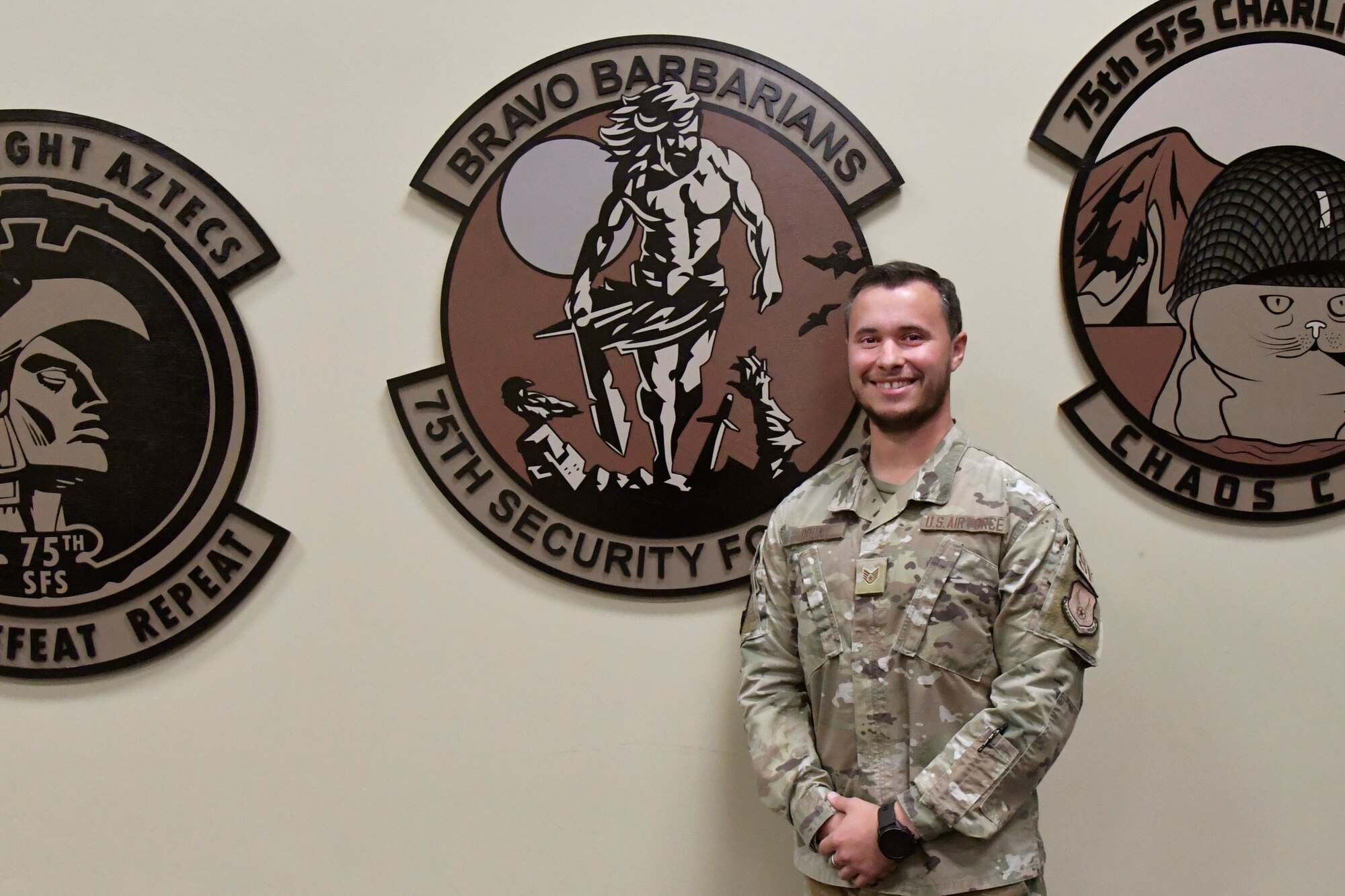 Staff Sgt. Roca stands next to a wall adorned with oversized squadron patches.
