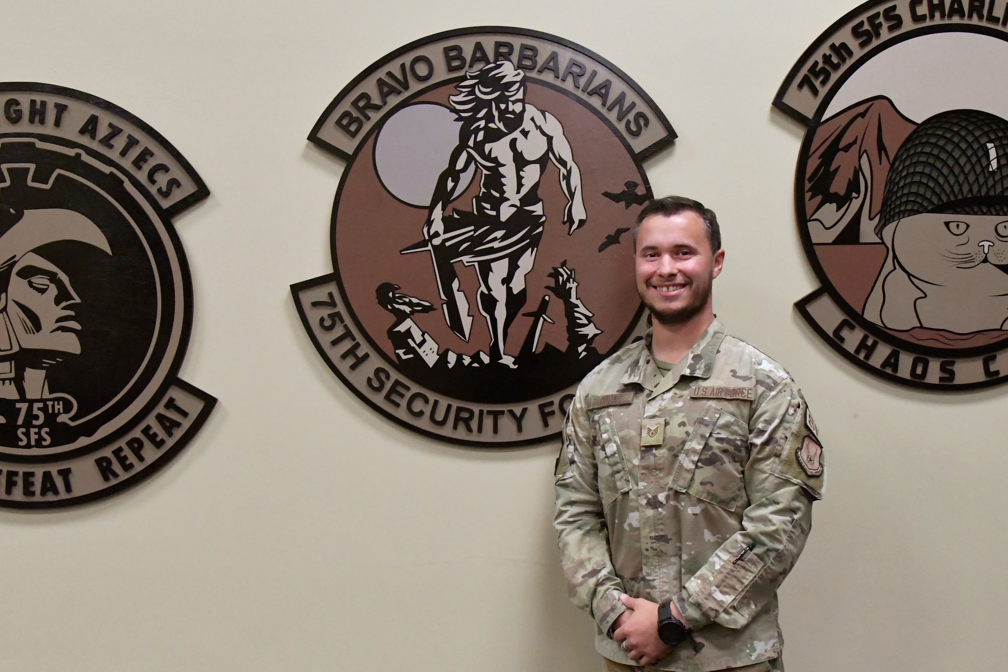 Staff Sgt. Roca stands next to a wall adorned with oversized squadron patches.