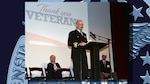 Photo is of a man in a Navy military uniform speaking from a podium during a Veterans Day ceremony.