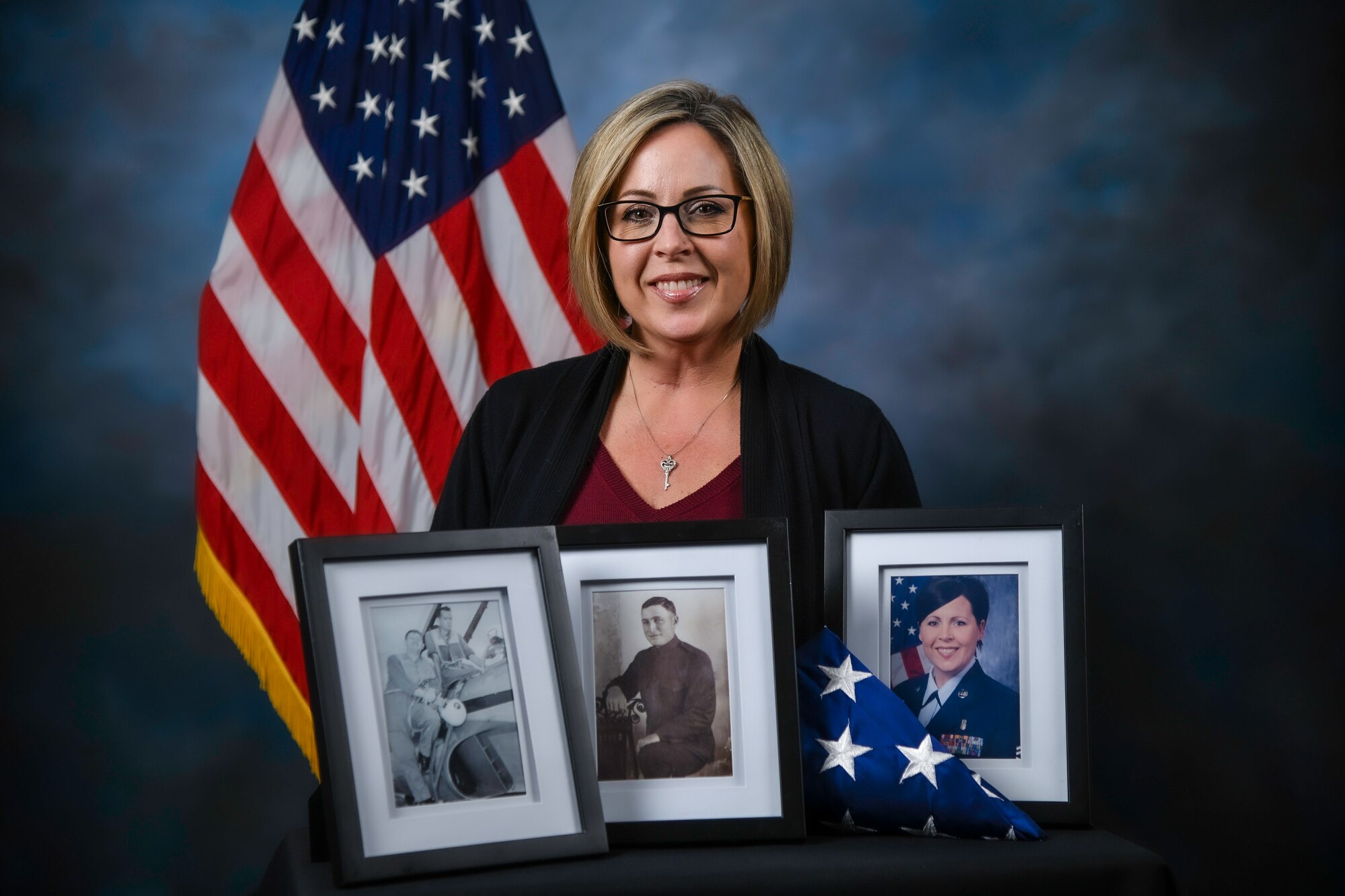 Woman poses for photo with portrait pictures and flag.