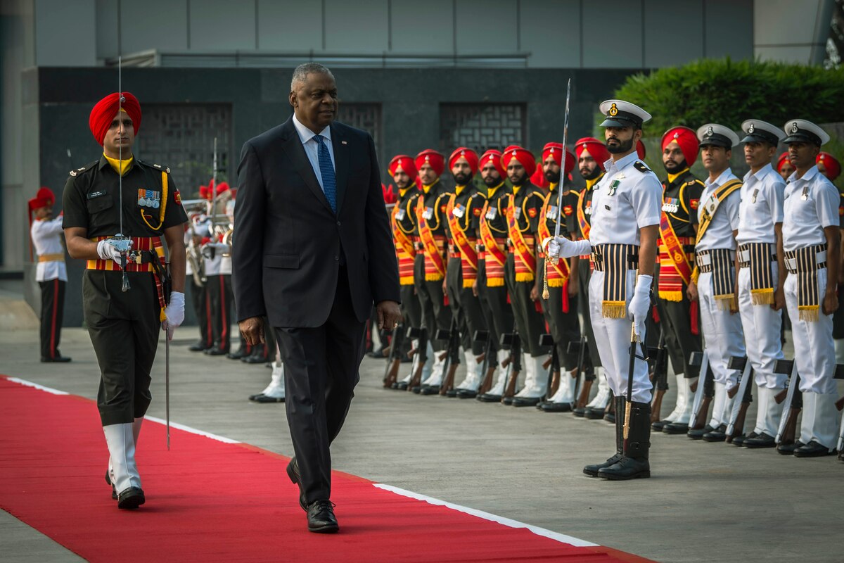 A person walks down a red carpet as military members stand in formation on the side.