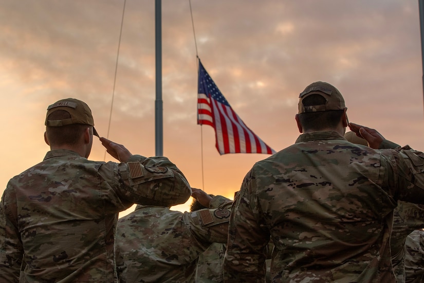 Military members salute flag as it's lowered in the evening.