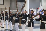 More than a dozen members of the Marine Corps Band Quantico play instruments in a semicircle in the McNamara Headquarters Complex cafeteria