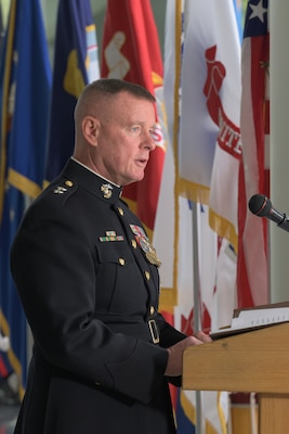 A profile view of Marine Corps Maj. Gen. David Maxwell speaking behind a lectern with military service flags in the background