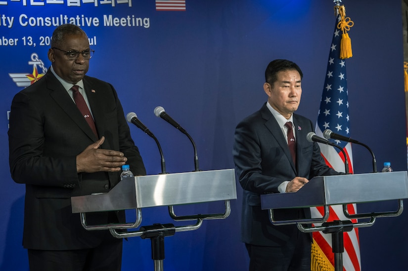 Two men in suits stand at lecterns.