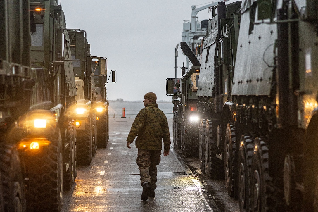 A Marine inspects two rows of vehicles lined up in a convoy.