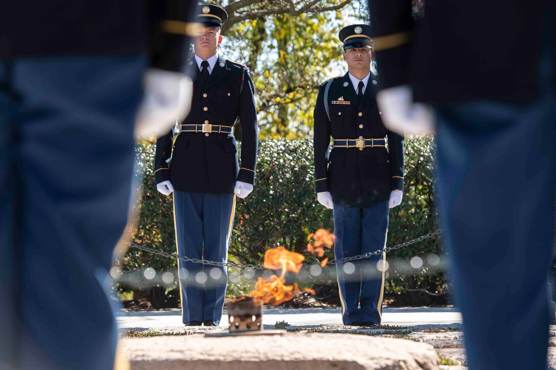 Soldiers stand in formation in front of a flame.