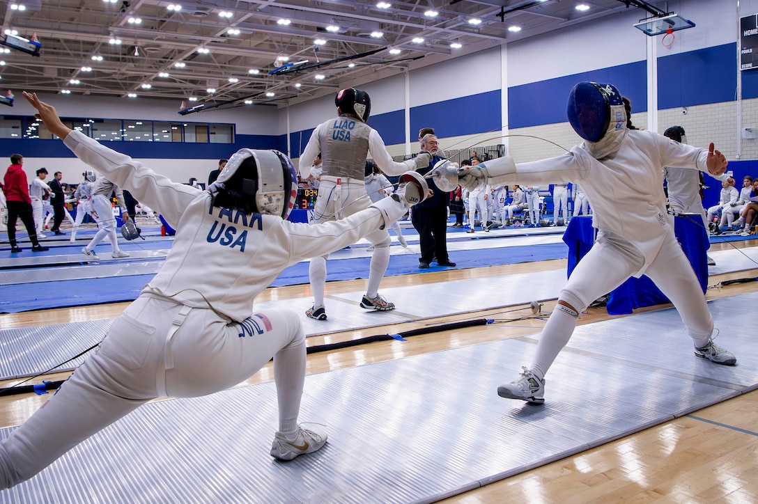 Two fencers holding swords and wearing protective masks lunge forward during a match as others compete in the background.