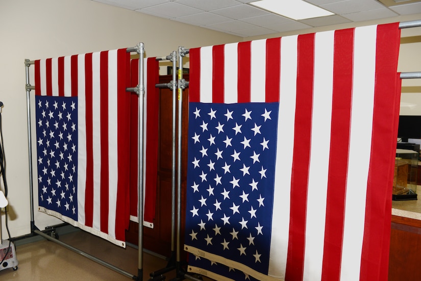 Three flags hang folded in half in a room.