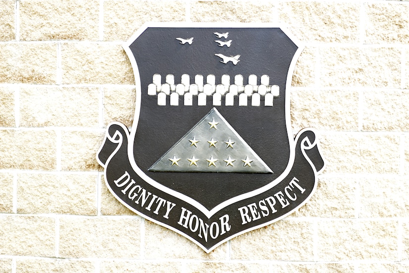 An emblem depicting graves, aircraft and a folded flag sits above a banner that reads, “dignity, honor, respect.”