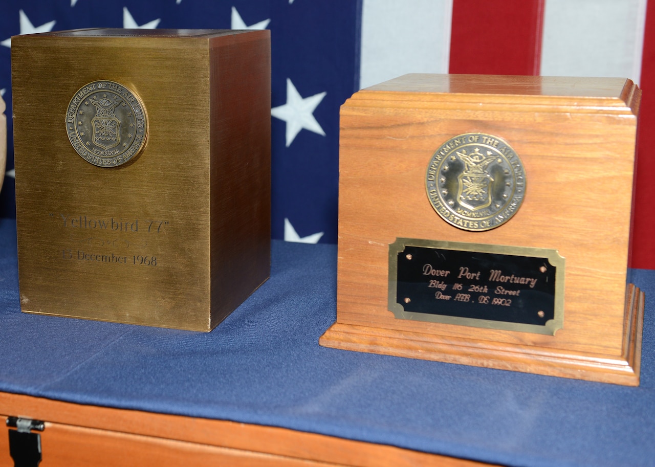 Two boxes, one wooden and one bronze, sit beside each other on a table.
