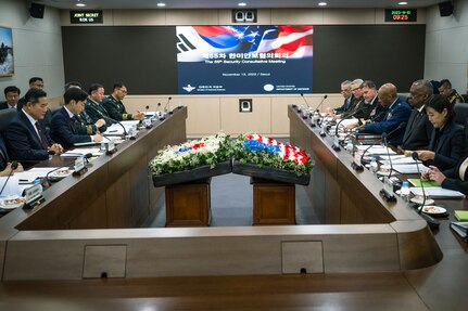 Men and women wearing business attire and military uniforms are seated at a table with flower displays that depict the U.S. and South Korean flags.
