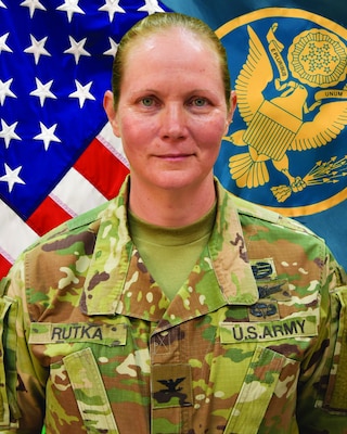 woman wearing army uniform standing in front of two flags.
