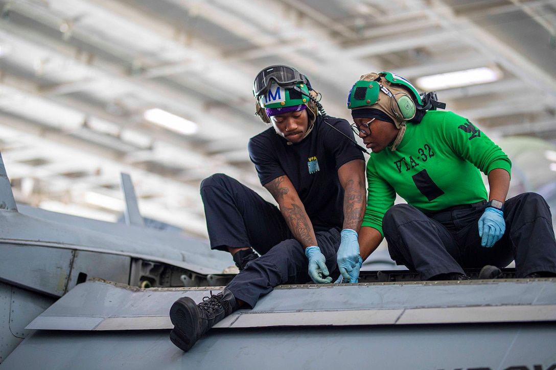 Two sailors conduct maintenance on an F/A-18F Super Hornet fighter jet.