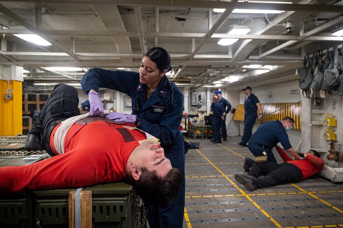 231109-N-ER894-2087 PHILIPPINE SEA (Nov. 9, 2023) Hospital Corpsman 1st Class Sandra Zapata, from North Brunswick, New Jersey, right, assesses the simulated injuries of Aviation Ordnanceman Airman Gabriel Tabarez, from Paso Robles, California, during a mass casualty drill in a weapons magazine aboard the U.S. Navy’s only forward-deployed aircraft carrier, USS Ronald Reagan (CVN 76), in the Philippine Sea, Nov. 9. Ronald Reagan, the flagship of Carrier Strike Group 5, provides a combat-ready force that protects and defends the United States, and supports alliances, partnerships and collective maritime interests in the Indo-Pacific region. (U.S. Navy photo by Mass Communication Specialist 3rd Class Timothy Dimal)