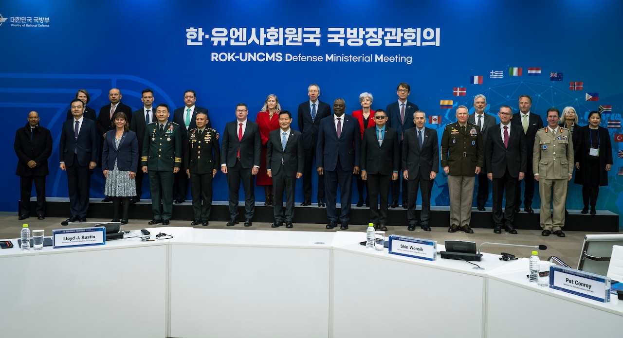 Women and men wearing suits and military uniforms pose for a photo.