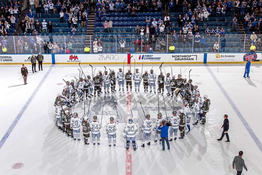 Hockey players form a circle at center ice and lift their sticks.