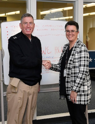 Two people shake hands and pose for a photo in an office space.