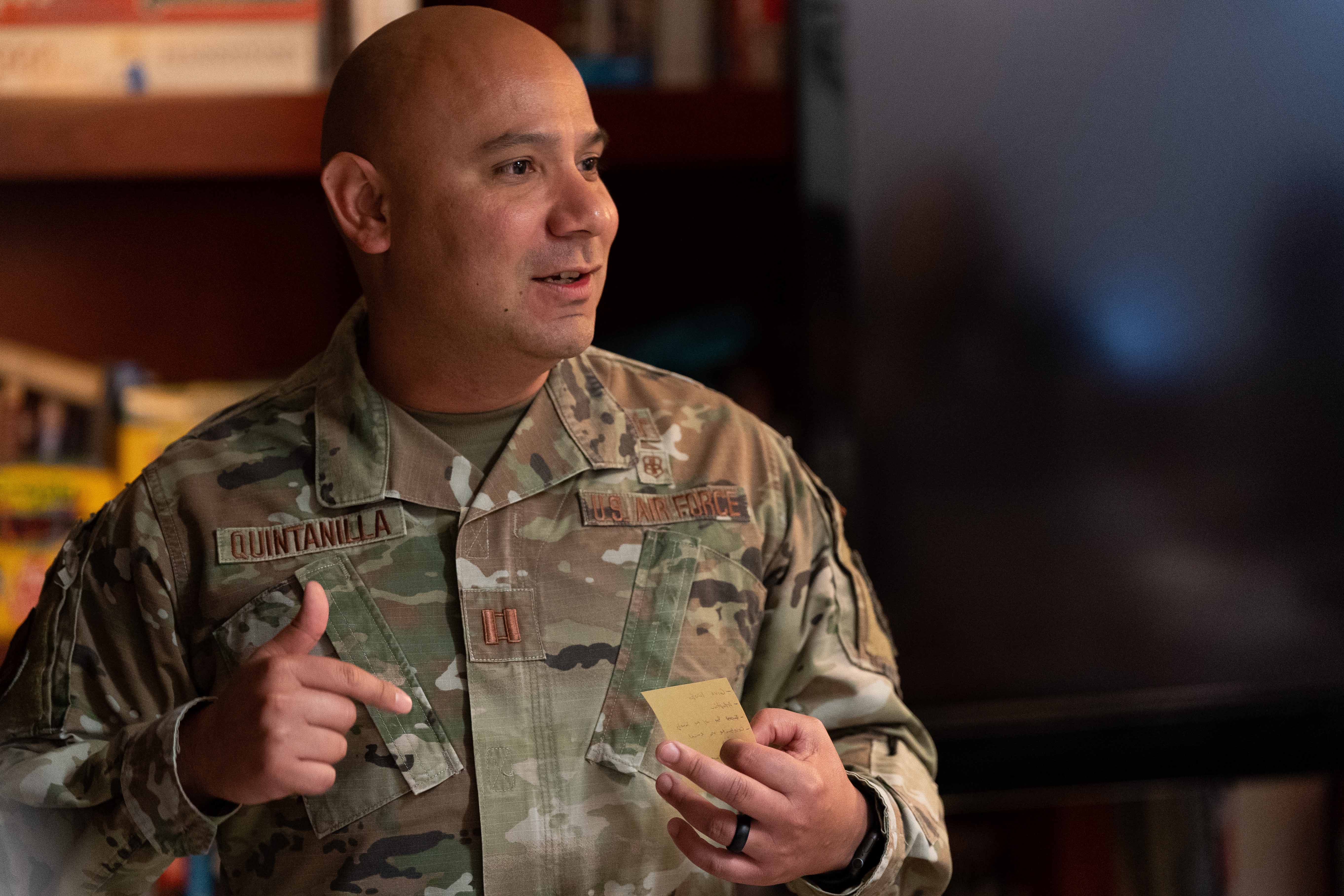 A person in uniform gestures with his hands while holding a small note.