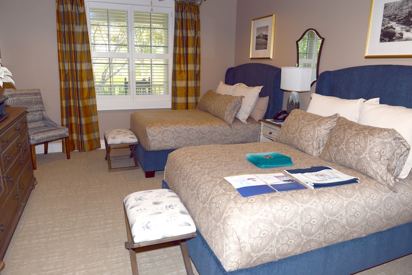 Two double beds with plush pillows are the centerpiece in a room with a window.